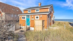 Una casa a due piani con una porta blu, una recinzione in legno e vista sul mare.