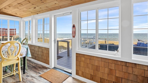 Una casa sulla spiaggia con ampie finestre che si affacciano sull'oceano, soffitto in legno e patio coperto.
