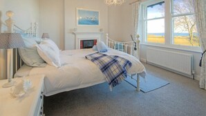 A bedroom with a bed, a nightstand, a lamp, a fireplace, and a window with a view. - The Villas No3 (Alnwick)