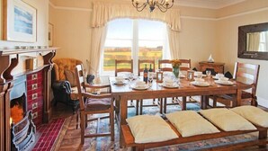 A dining room with a large wooden table set for six, flanked by chairs, a fireplace, and a view of the countryside. - The Villas No3 (Alnwick)