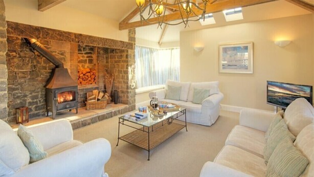 A cozy living room with a stone fireplace, white sofas, a glass coffee table, and a large window with curtains. - The Villas No3 (Alnwick)