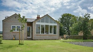 Et toetagers hus med et stort glasvindue foran, en velholdt græsplæne og en stenvæg i baggrunden.