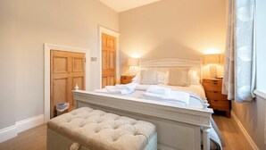 Une chambre avec un grand lit, des lampes de chevet, une porte en bois et un petit banc.