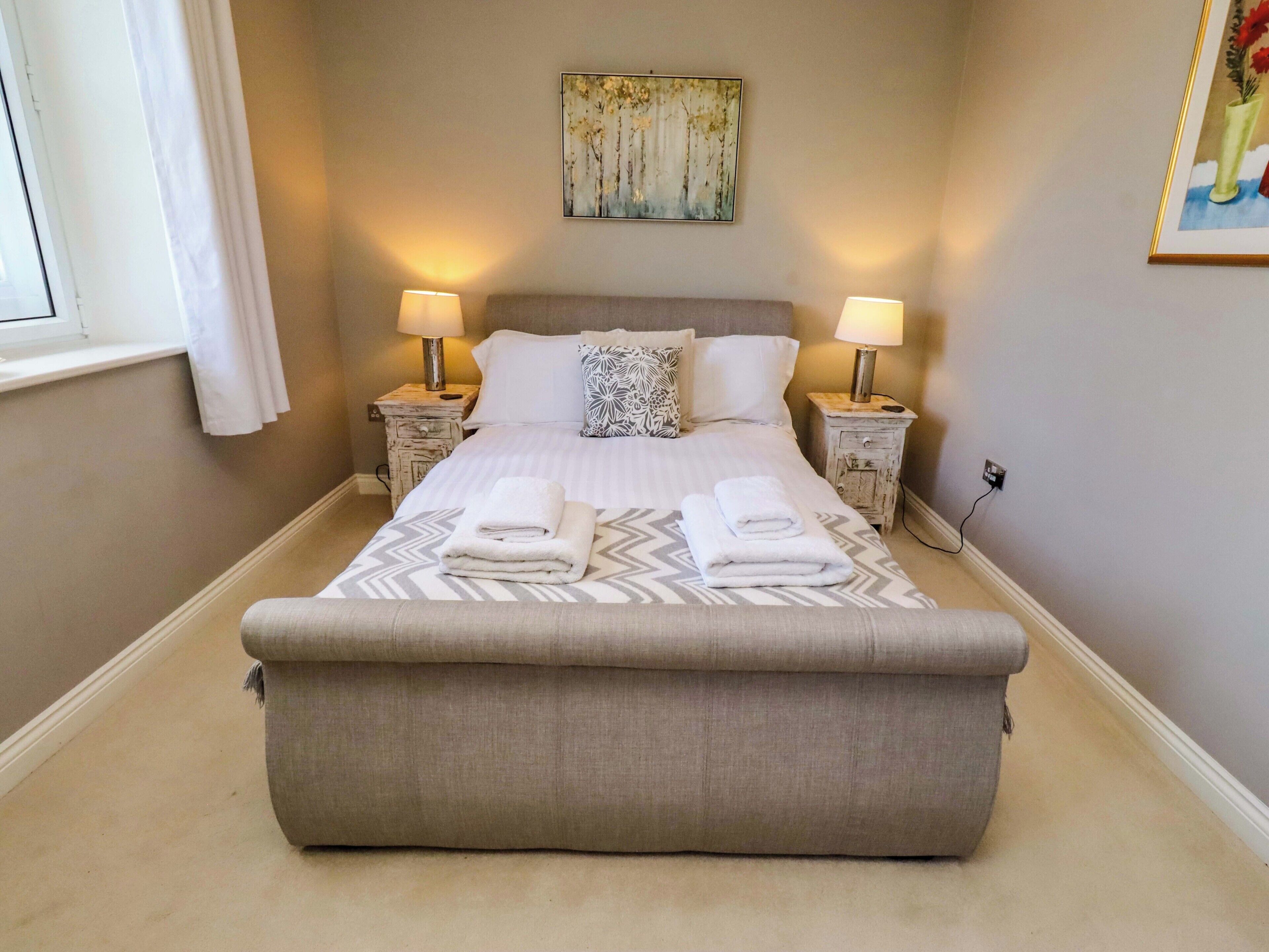 A neatly made bed with two pillows, a bedside table with a lamp, and a painting on the wall.
