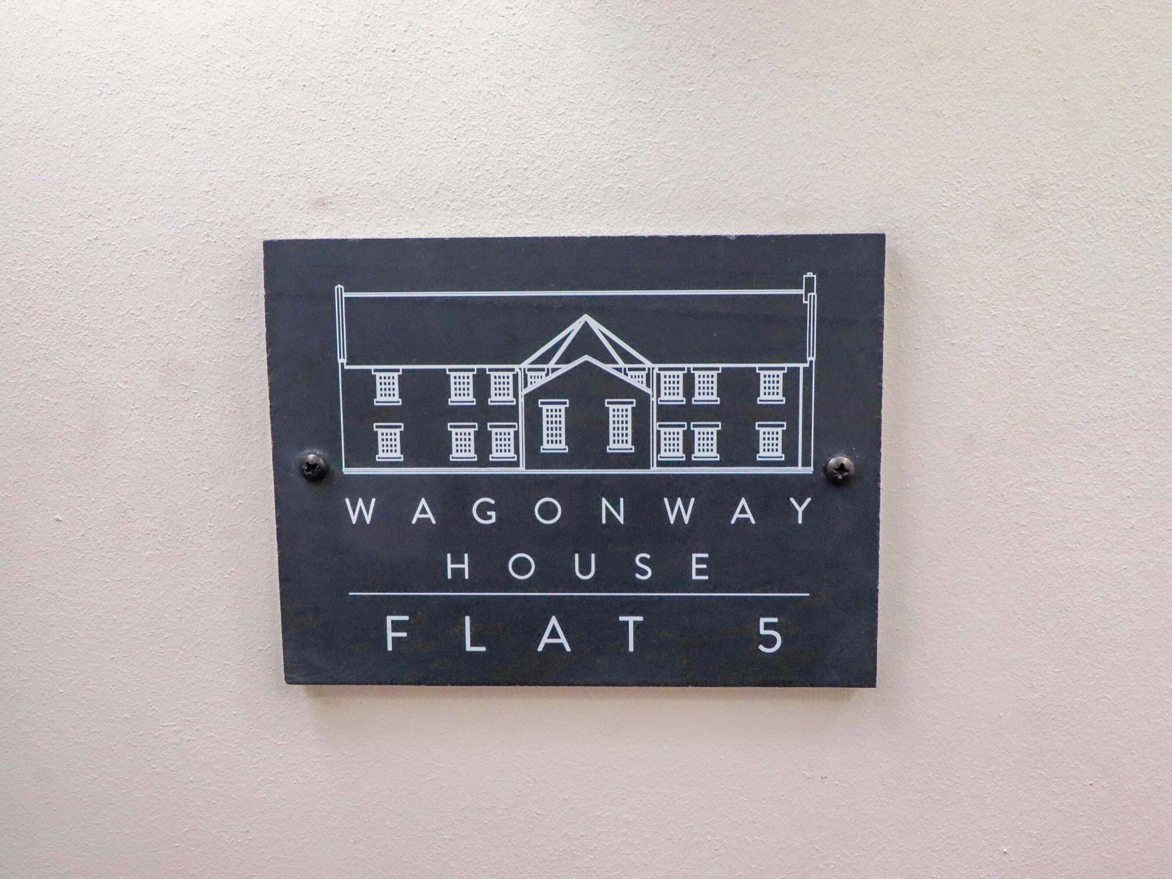 A sign with a building illustration and text 'WAGONWAY HOUSE FLAT 5' on a wall.