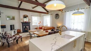 A spacious kitchen with a large island, wooden beams on the ceiling, a fireplace, and a dining area with a sofa. - Treetops, Alnwick (Alnwick)