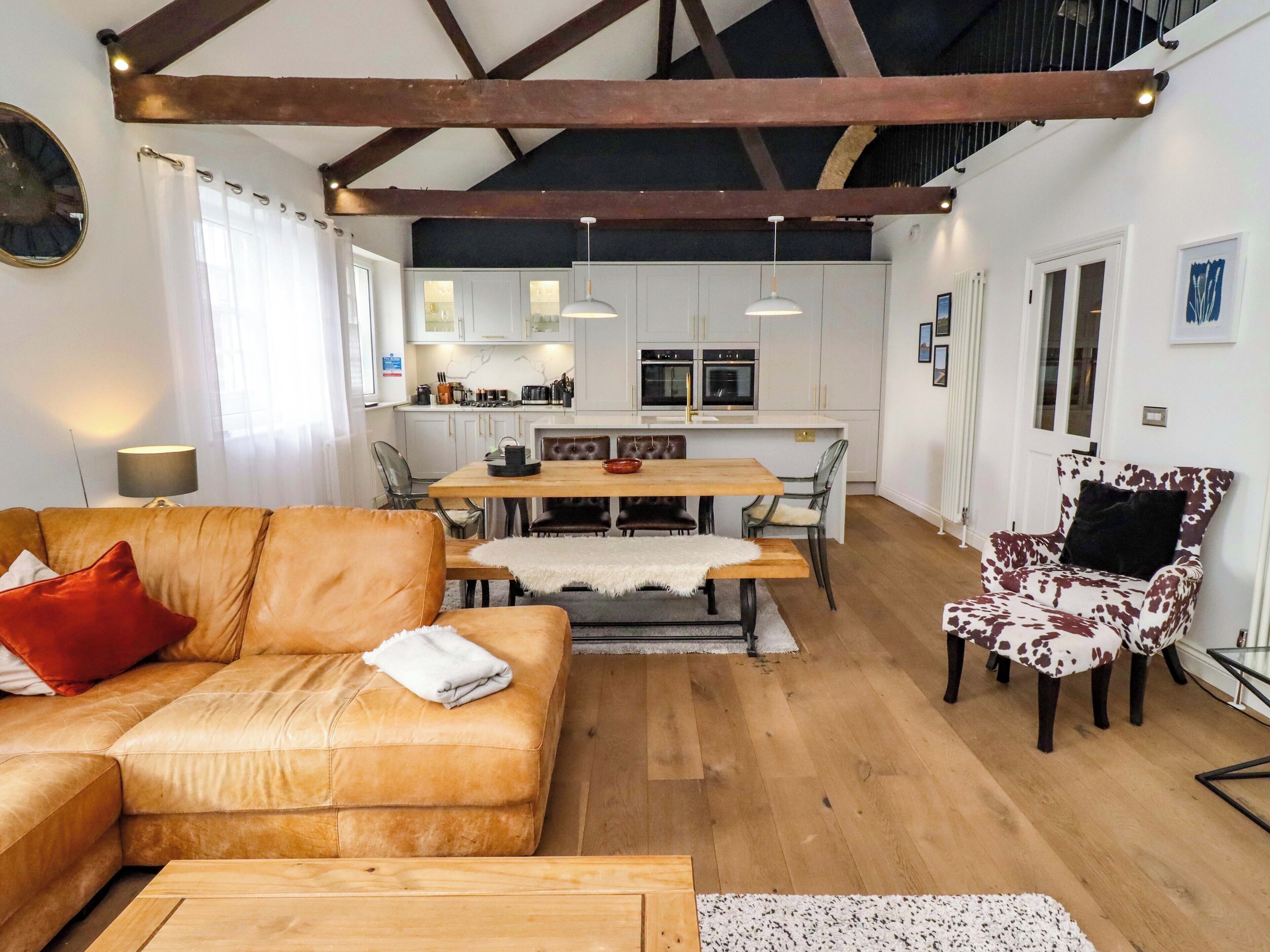 A modern living room with a wooden sofa, a dining table, and a kitchen in the background.