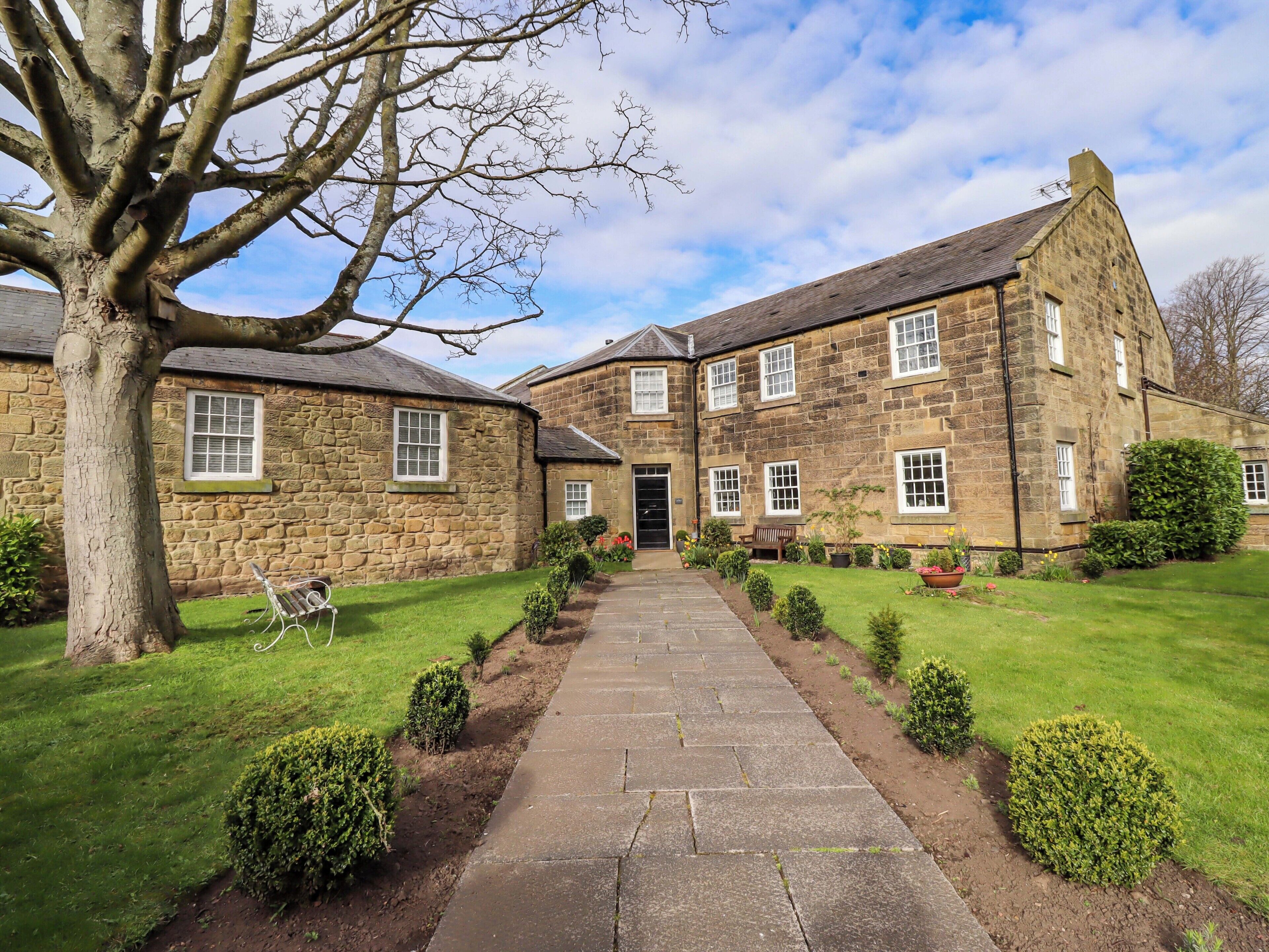 A stone building with a central entrance, a paved pathway, and well-maintained lawns.