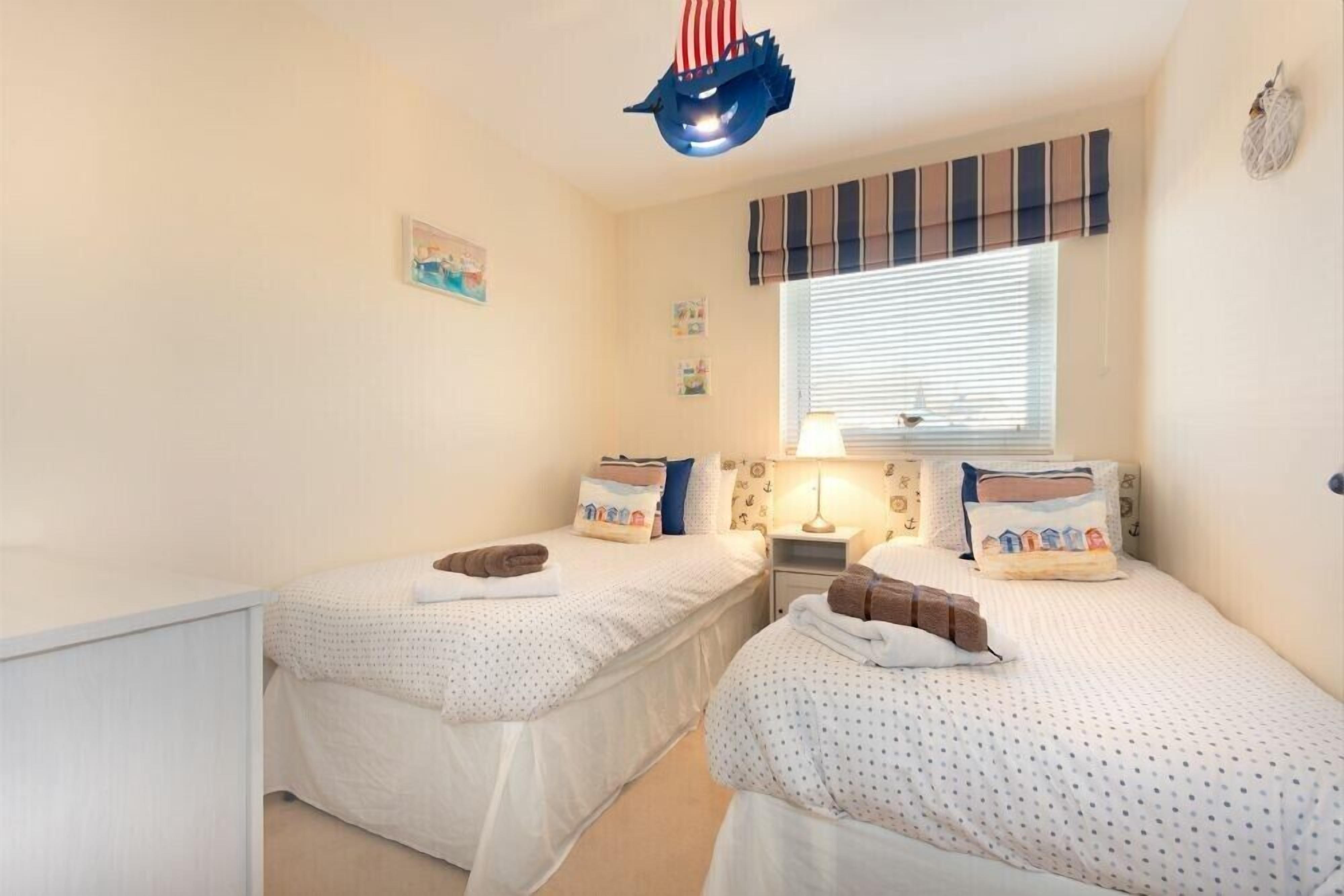 Ein Zimmer mit zwei Betten, einem Fenster mit Jalousien, einer Lampe und einer Zierleuchte an der Decke.