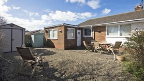 A residential property with a gravel driveway, a detached garage, a brick extension, and a patio with outdoor furniture.