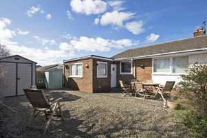 A residential property with a gravel driveway, a detached garage, a brick extension, and a patio with outdoor furniture.