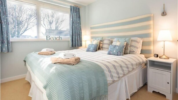 A bedroom with a striped headboard, a bed with a striped bedspread, two bedside lamps, and a window with curtains.