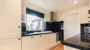 A modern kitchen with white cabinets, black countertops, a stainless steel range hood, and a window with a view of a brick building.
