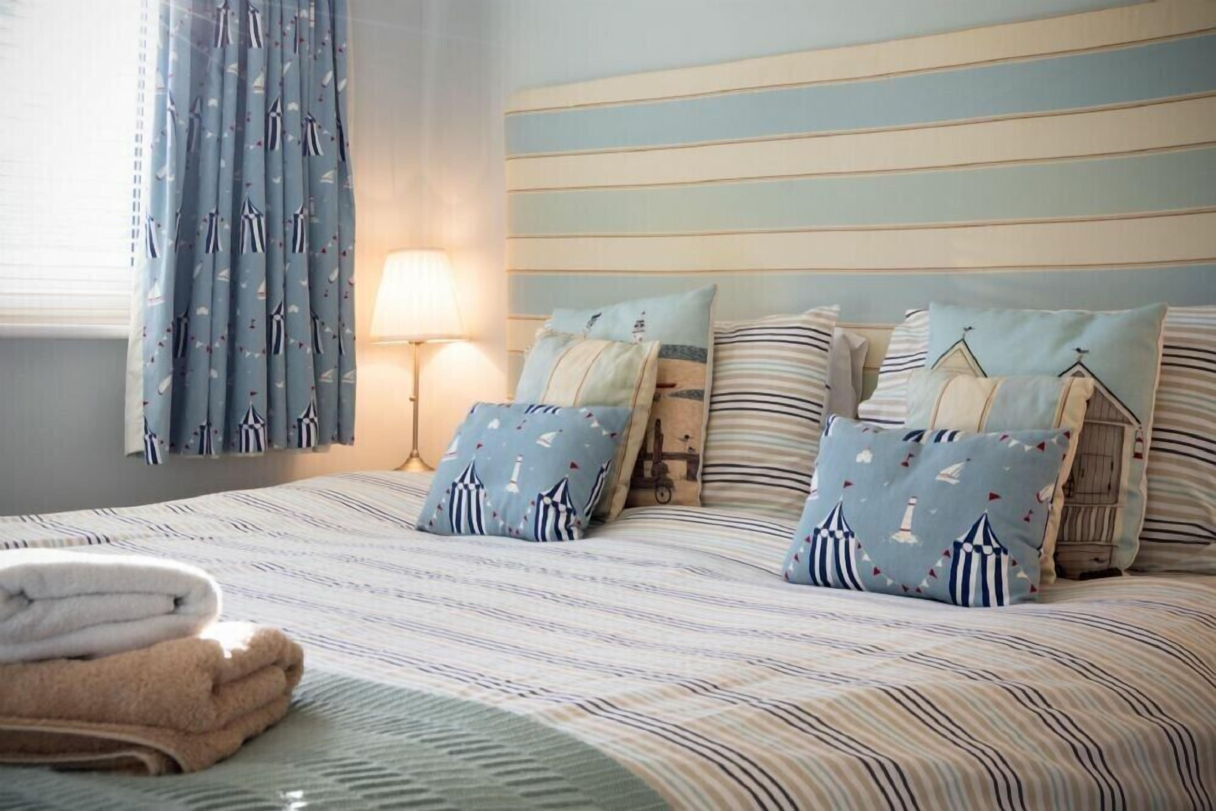 A neatly made bed with striped bedding and matching pillows, a bedside lamp, and a window with curtains.
