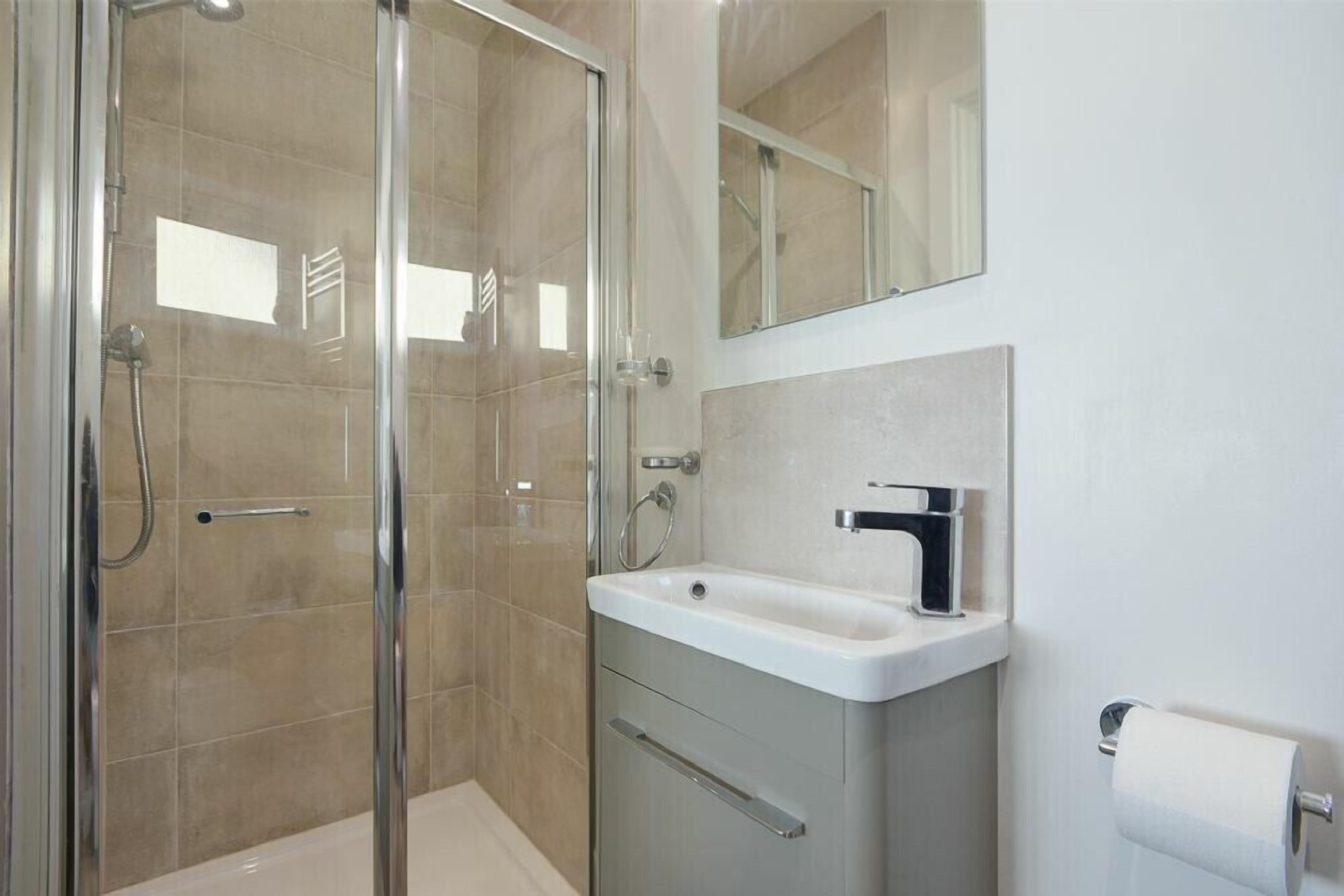 Un bany modern amb dutxa envidrada amb vidre, un lavabo blanc i un mirall sobre el lavabo.