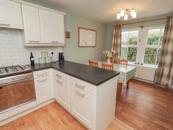 A kitchen with white cabinets, a gas stove, a coffee maker, and a dining area with a table and chairs.
