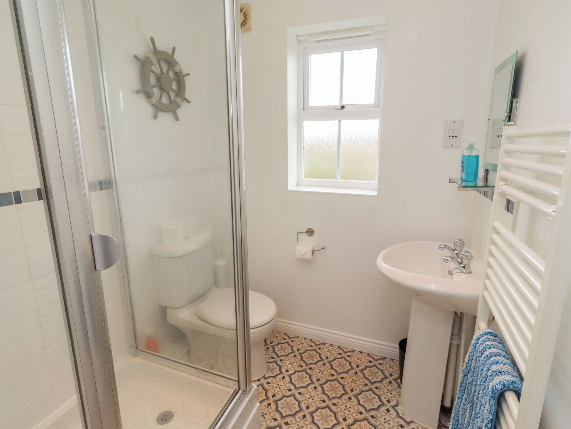A bathroom with a glass shower enclosure, a toilet, a sink, and a window.