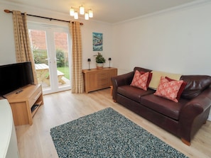 A living room with a TV, wooden cabinet, leather sofa, and a green rug.