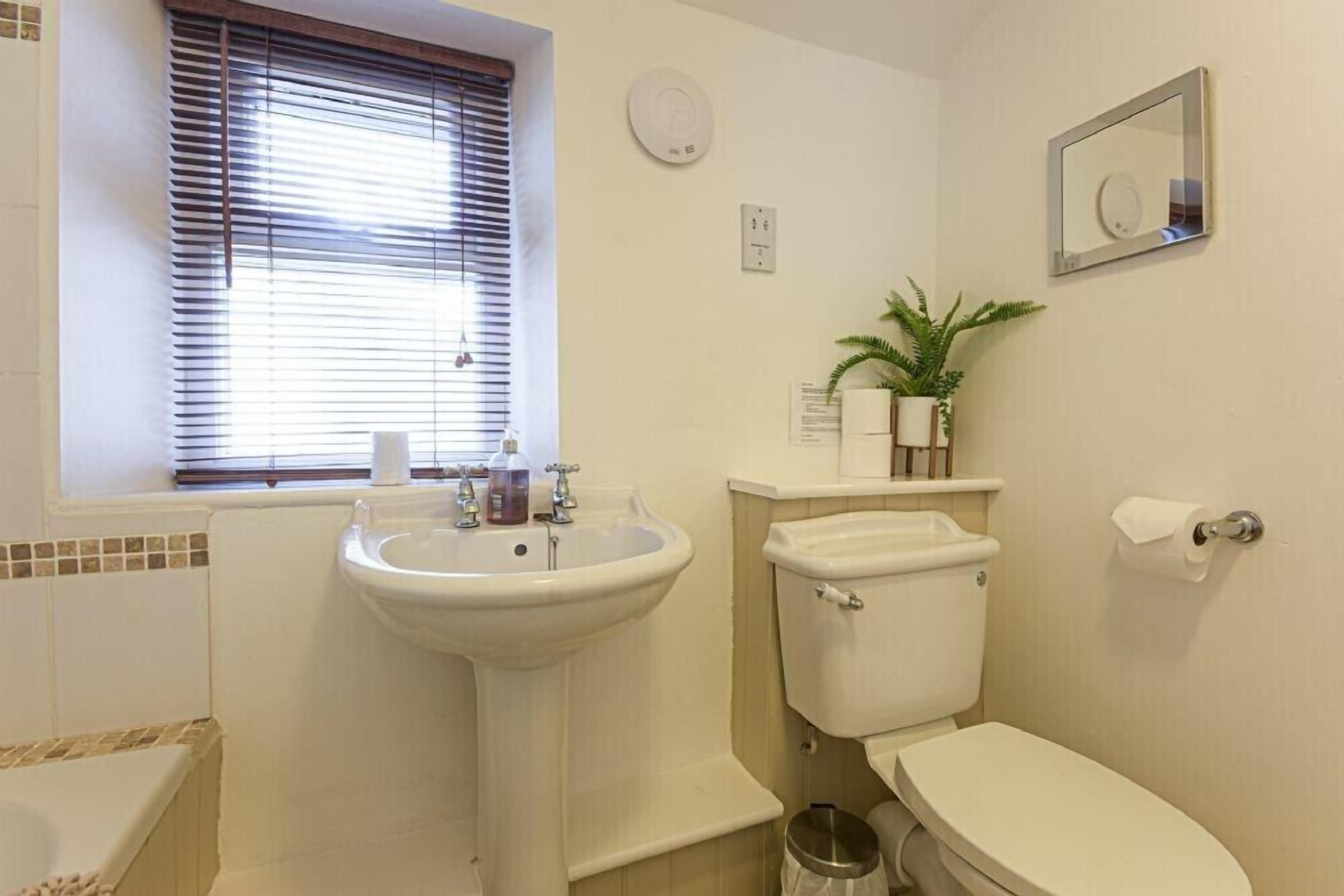 A bathroom with a sink, toilet, and window with blinds.