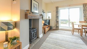 A cozy living room with a fireplace, a television, and a dining area with a view through large windows.