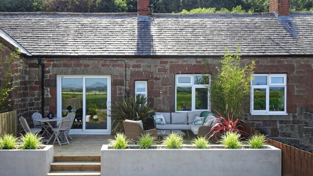 A stone house with a patio, outdoor seating, and a view of the countryside.