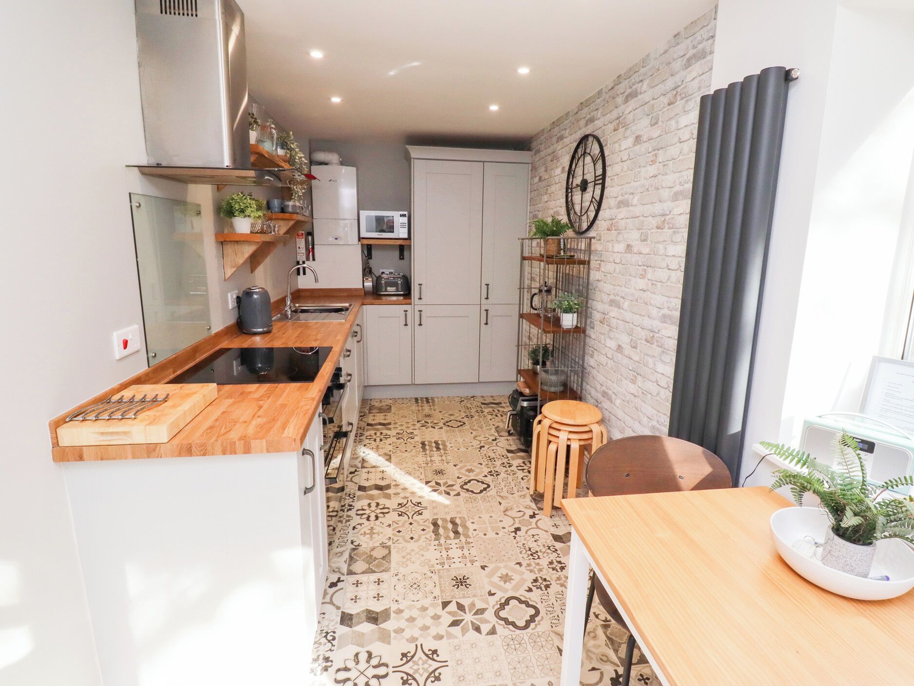Una cocina compacta con encimera de madera, armarios blancos y suelo estampado.