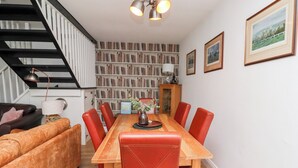 A dining area with a wooden table and red chairs, a bookshelf in the background, and a staircase to the left.