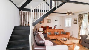 A staircase leading to a loft bedroom, a living room with a sofa and coffee table, and a dining area with chairs and a table.