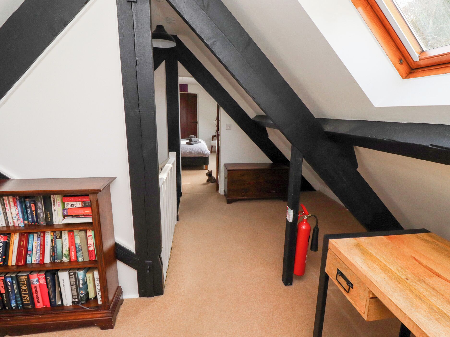 Un couloir étroit avec une bibliothèque en bois, un extincteur et une table en bois.