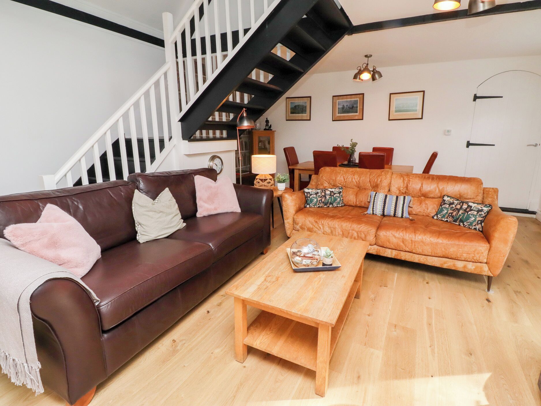 A living room with a brown leather sofa, a wooden coffee table, and a staircase with black railings.