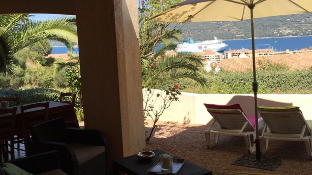 An outdoor seating area with wicker furniture, a table with a candle and tray, and a view of the sea and a cruise ship. - VILLA WITH HEATED POOL and ocean view - Margaux Villa (Propriano)
