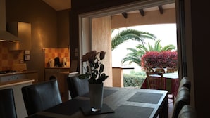 A dining area with a table set for four, a vase with flowers, and a view of a garden with palm trees and red foliage. - VILLA WITH HEATED POOL and ocean view - Margaux Villa (Propriano)