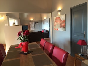 Un coin repas avec une table en bois, des chaises rouges et un vase rouge contenant des fleurs.