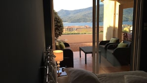 A room with a bed, a nightstand, a lamp, and a view of a balcony with outdoor furniture and a scenic landscape. - VILLA WITH HEATED POOL and ocean view - Margaux Villa (Propriano)