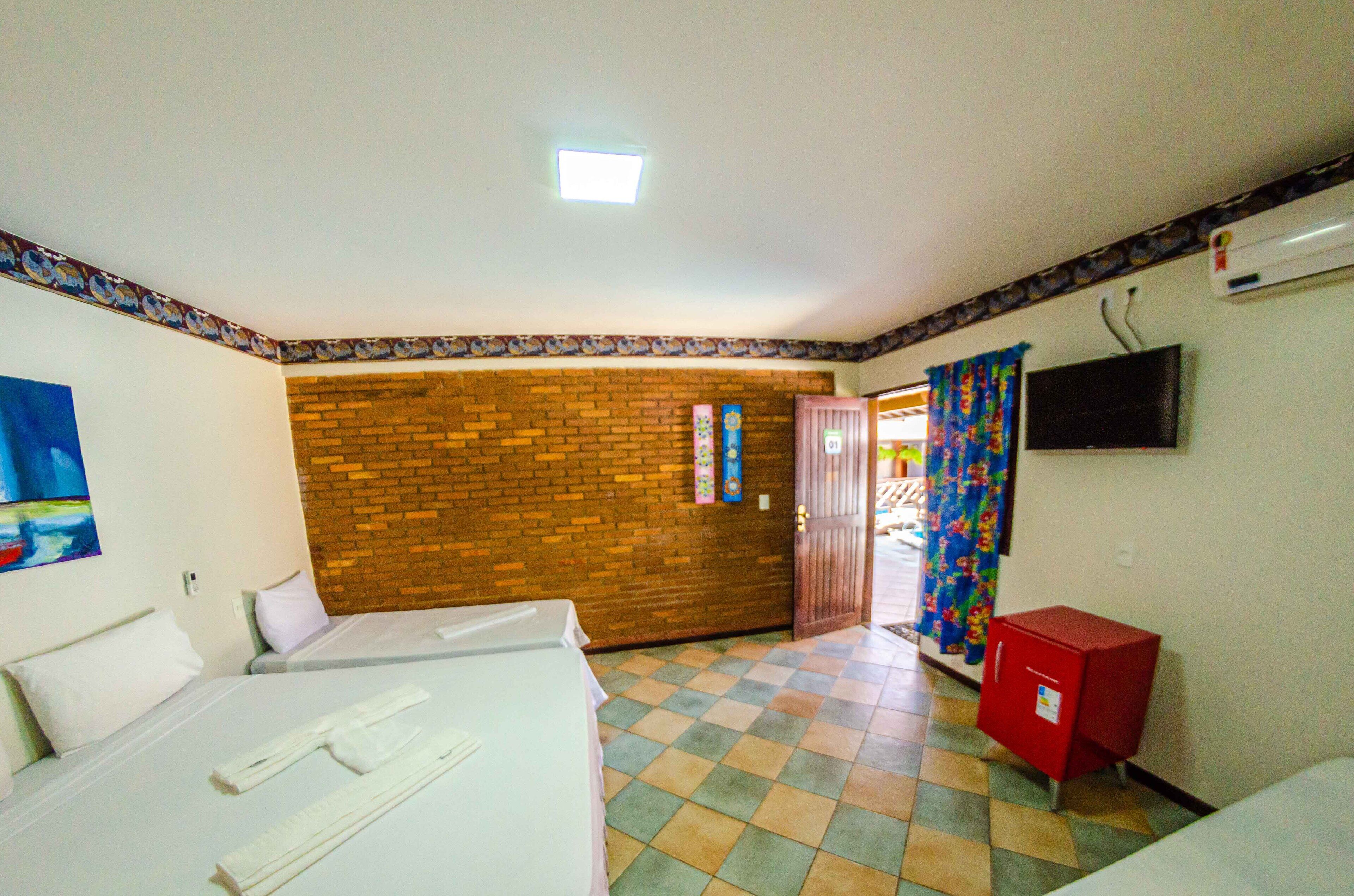 Hotellihuone, jossa on kaksi sänkyä, tiiliseinä, televisio ja punainen kaappi.