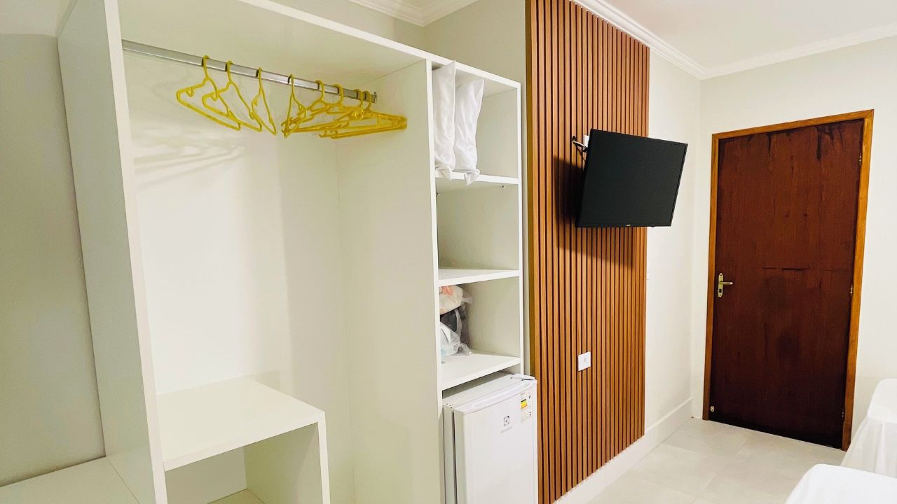 A room with a wardrobe, a television mounted on the wall, and a wooden door.