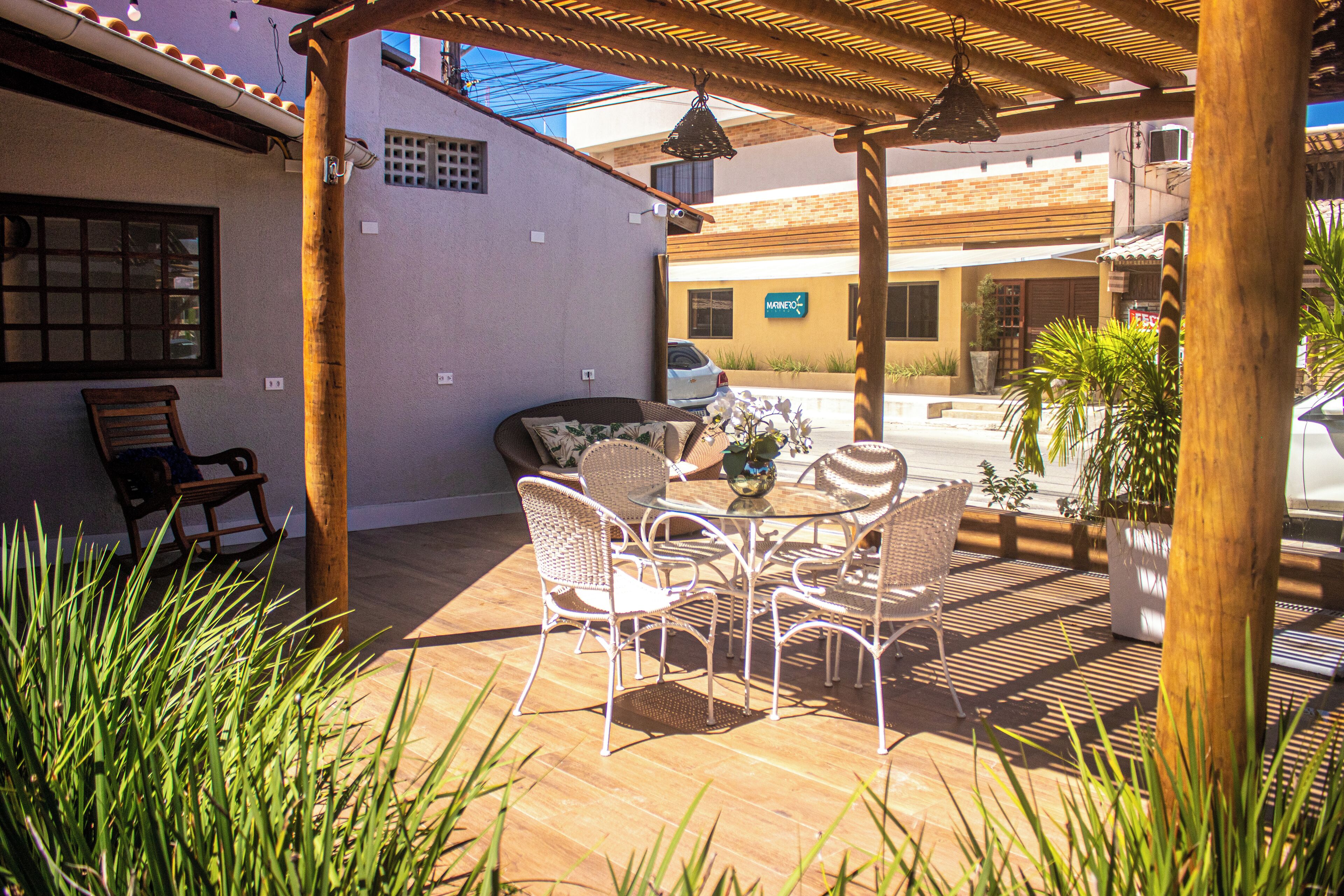 An outdoor patio with a wooden pergola, wicker chairs, and a table with a vase.