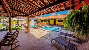 Un espacio al aire libre cubierto con una piscina, asientos y un edificio de techo con tejas.