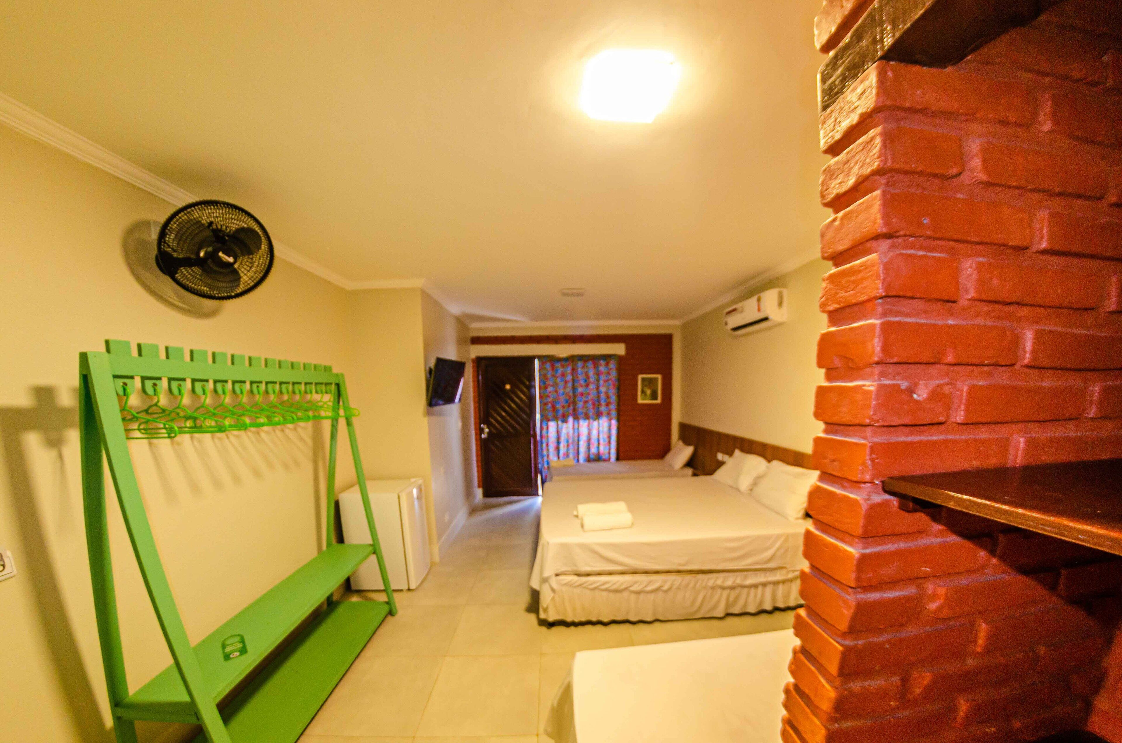 A hotel room with a brick fireplace, a green bench, a bed with a white comforter, and a wall-mounted fan.