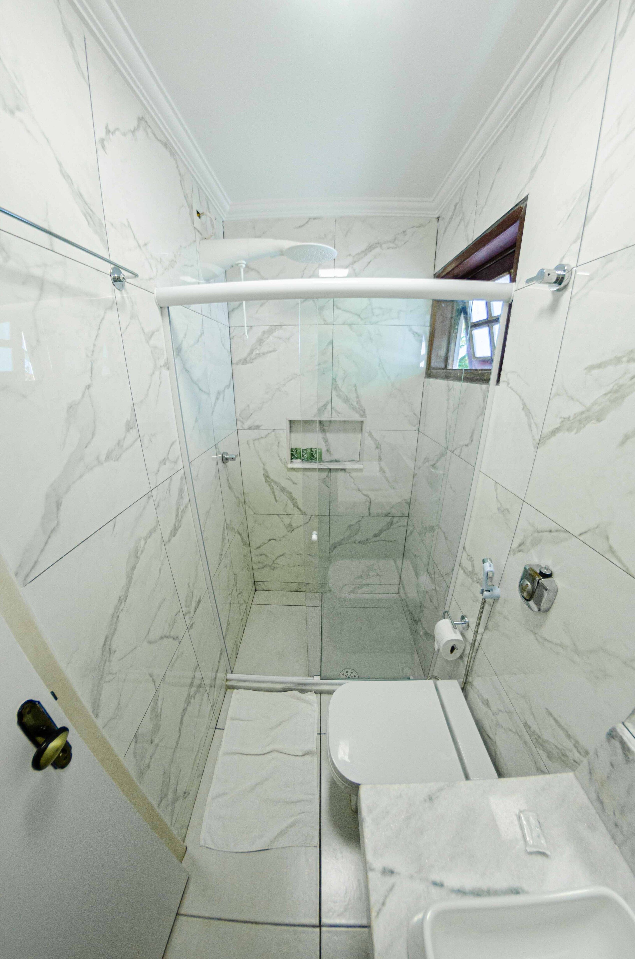 Un baño con ducha, inodoro y lavamanos, todo con paredes y suelo de mármol.