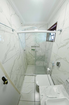 Un baño con ducha, inodoro y lavamanos, todo con paredes y suelo de mármol.