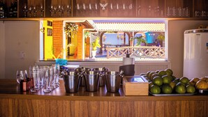 Una zona de bar con mostrador de madera, diversas botellas, vasos y vista del patio exterior.