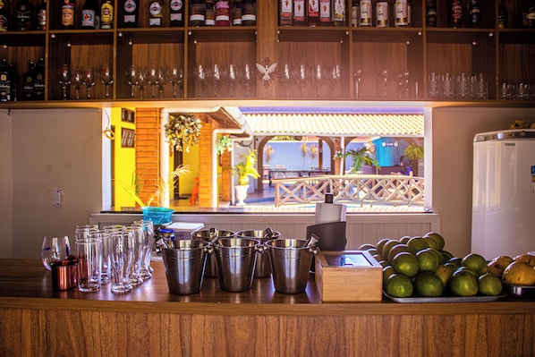 Una zona de bar con mostrador de madera, diversas botellas, vasos y vista del patio exterior.