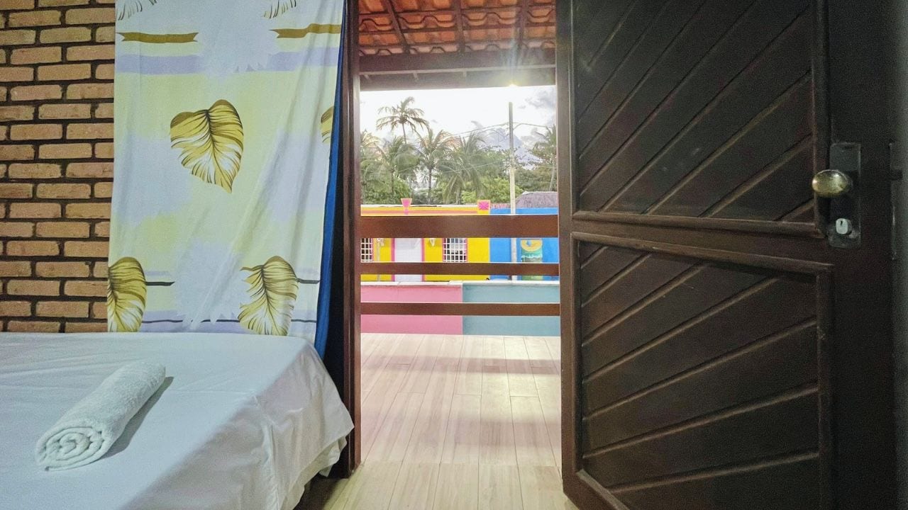 A room with a bed, a window with a curtain, and a view of a colorful building outside.