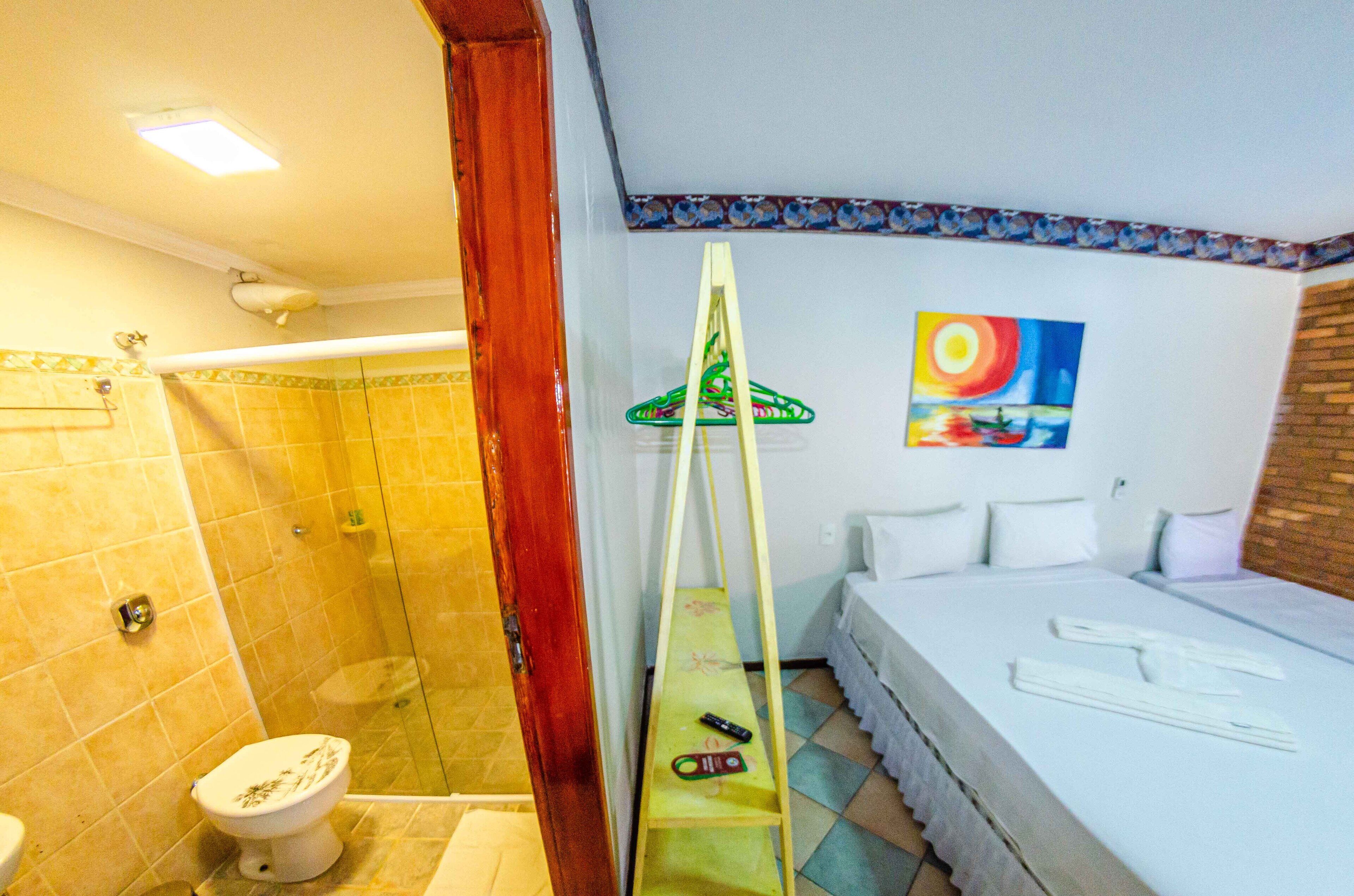 A bathroom with a shower, toilet, and a bed with towels and a painting on the wall.