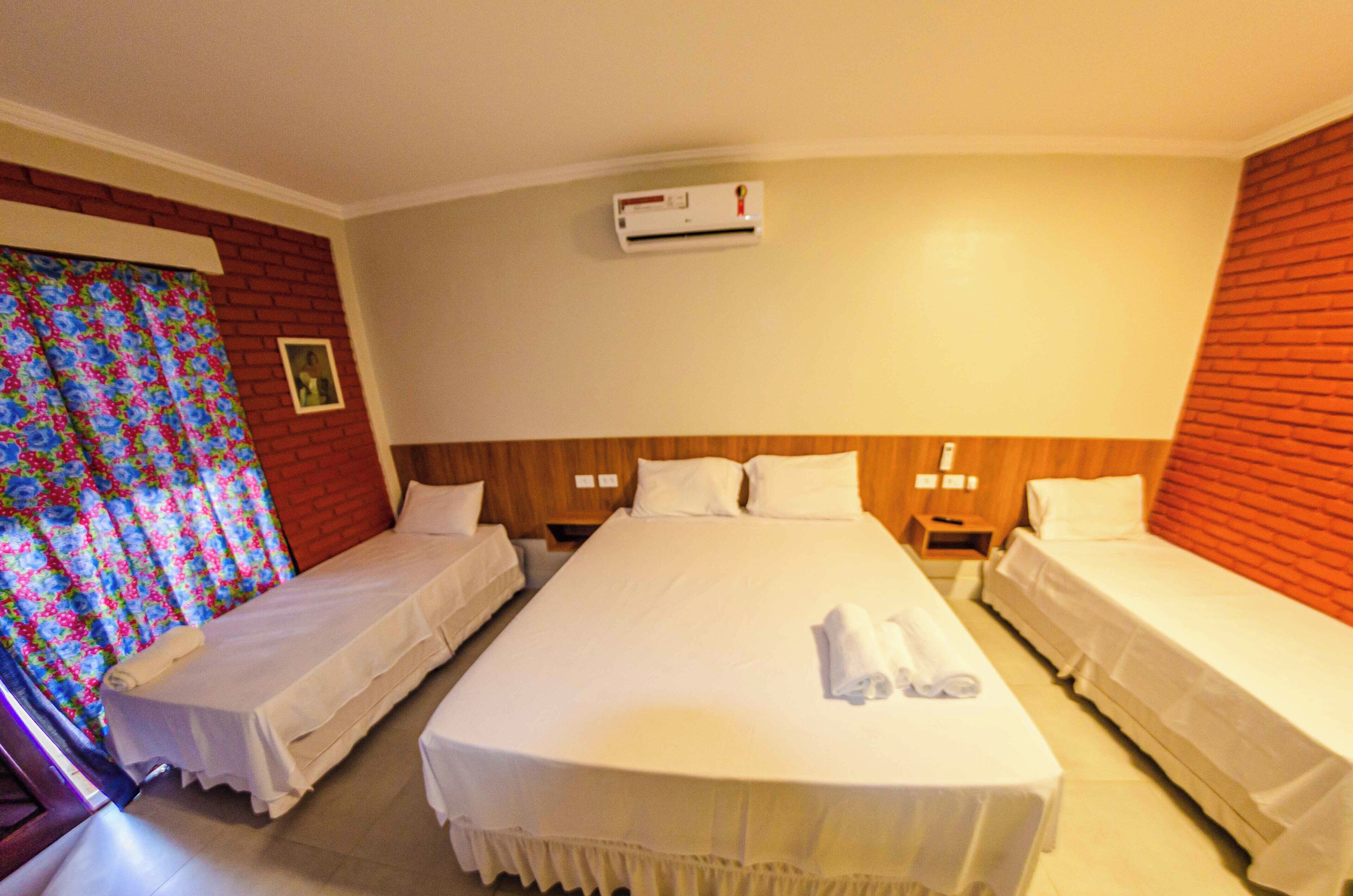 Une chambre d’hôtel avec deux lits simples, un lit plus grand et un appareil de climatisation fixé au mur.