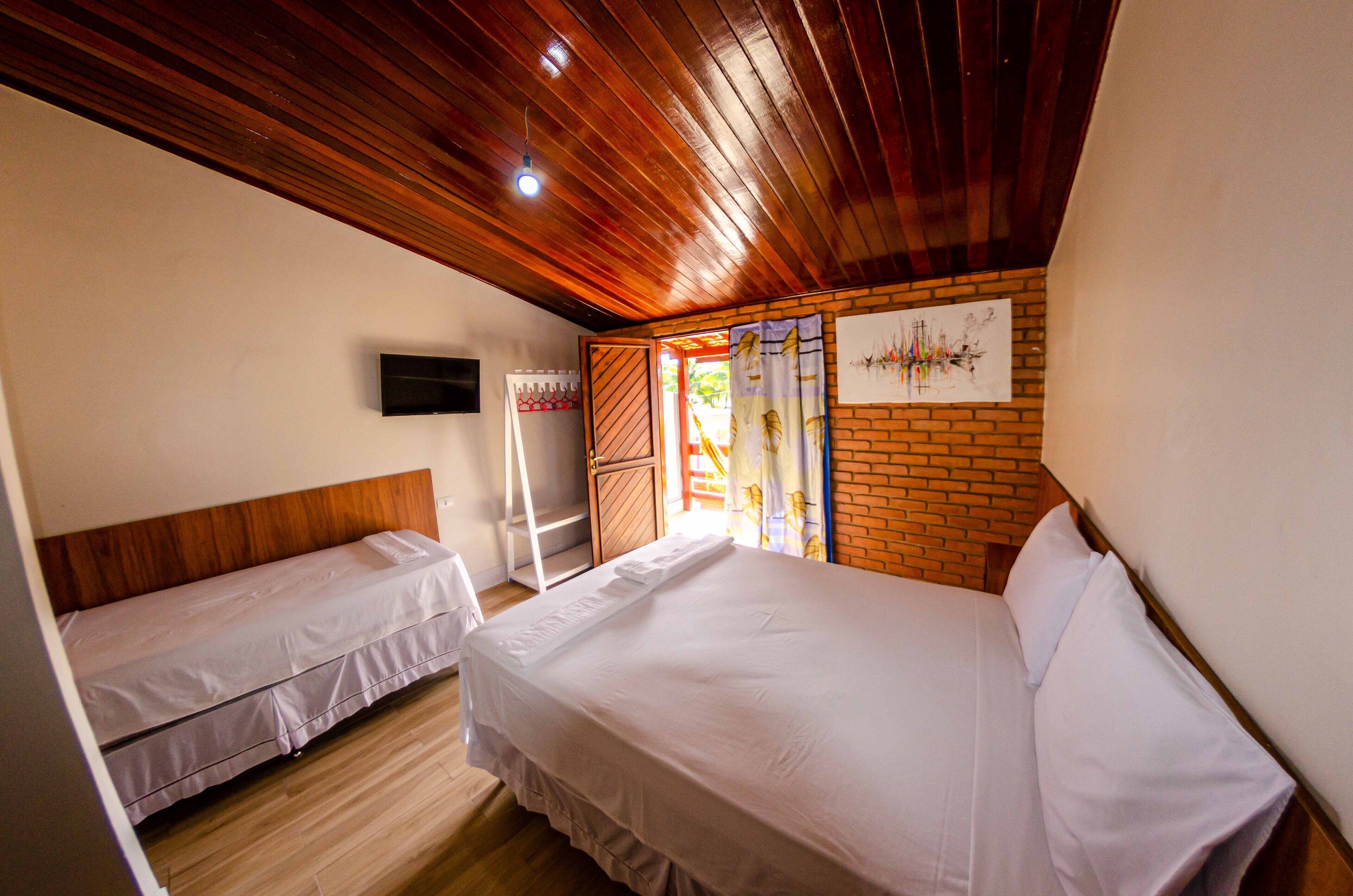 Une chambre avec deux lits, un plafond en bois, un mur en briques et un téléviseur fixé au mur.