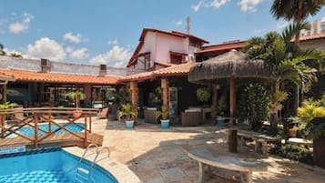 Un espace piscine doté d’une terrasse en bois, de chaises longues et d’un parasol en chaume.