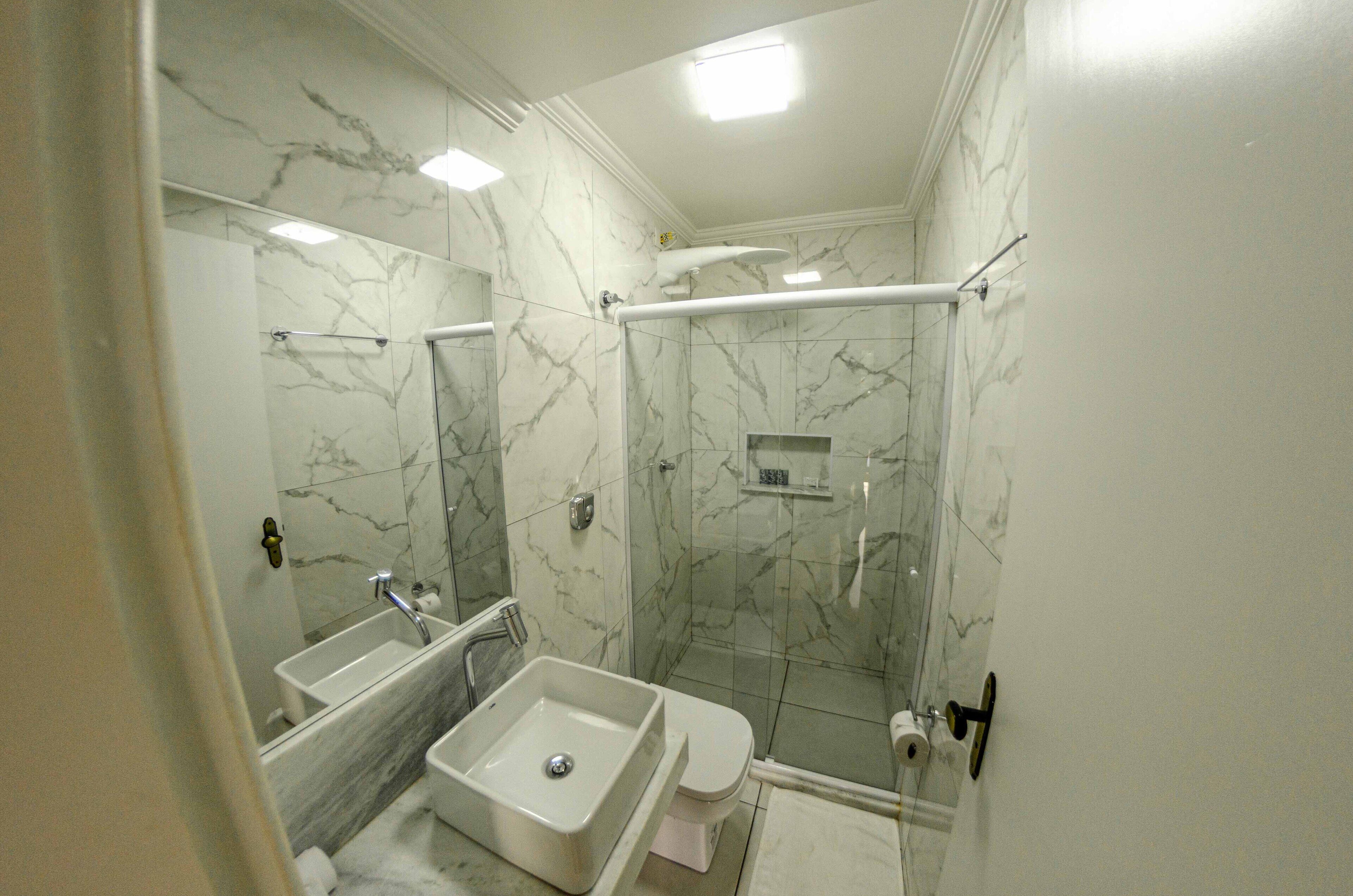 A bathroom with a marble wall, a sink, a toilet, and a glass-enclosed shower.
