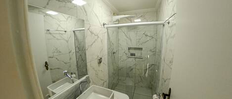 A bathroom with a marble wall, a sink, a toilet, and a glass-enclosed shower.